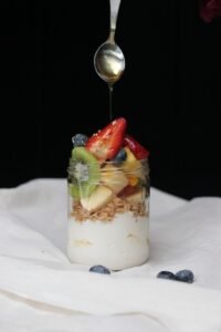 a spoon drizzling fruit into a jar of yogurt