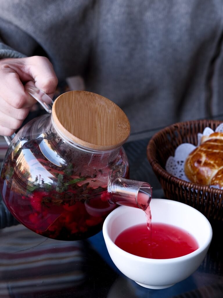 A person pours tea into a glass pitcher